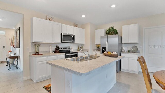 kitchen with light tile patterned floors, an island with sink, stainless steel appliances, sink, and white cabinetry