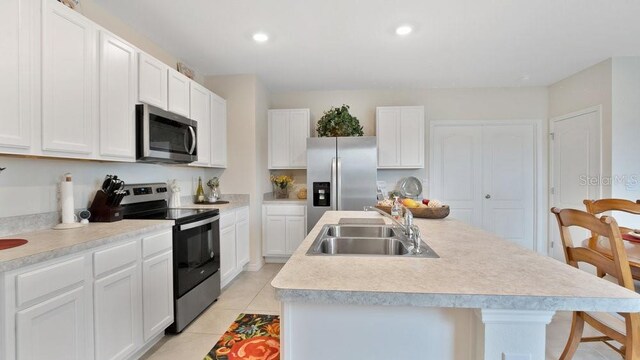 kitchen featuring light tile patterned flooring, stainless steel appliances, sink, and a kitchen island with sink