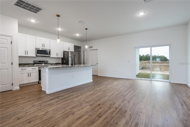 kitchen featuring stainless steel appliances, an island with sink, wood-type flooring, white cabinetry, and stone counters