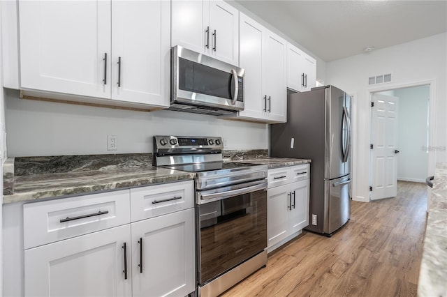 kitchen with appliances with stainless steel finishes, dark stone countertops, white cabinetry, and light hardwood / wood-style floors