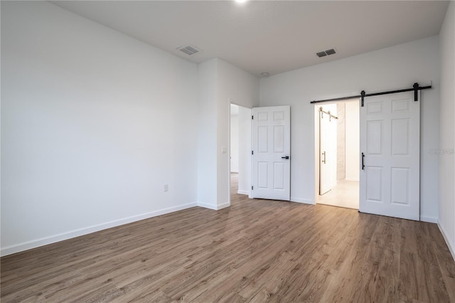 unfurnished bedroom featuring a barn door and hardwood / wood-style flooring