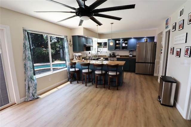 kitchen featuring kitchen peninsula, wood-type flooring, stainless steel refrigerator, and blue cabinetry