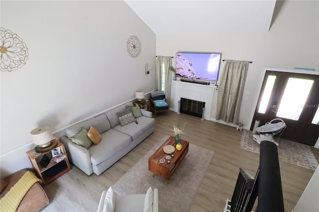 living room with light hardwood / wood-style floors, high vaulted ceiling, and french doors