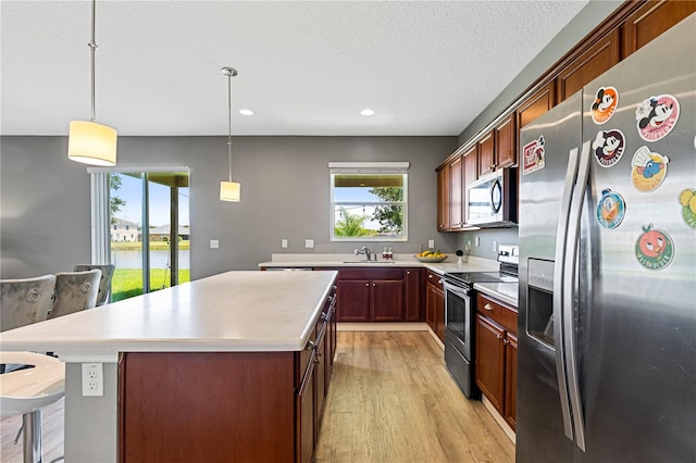 kitchen featuring light wood-type flooring, appliances with stainless steel finishes, pendant lighting, and a kitchen island