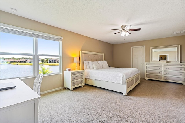 bedroom with a textured ceiling, ceiling fan, a water view, and light colored carpet