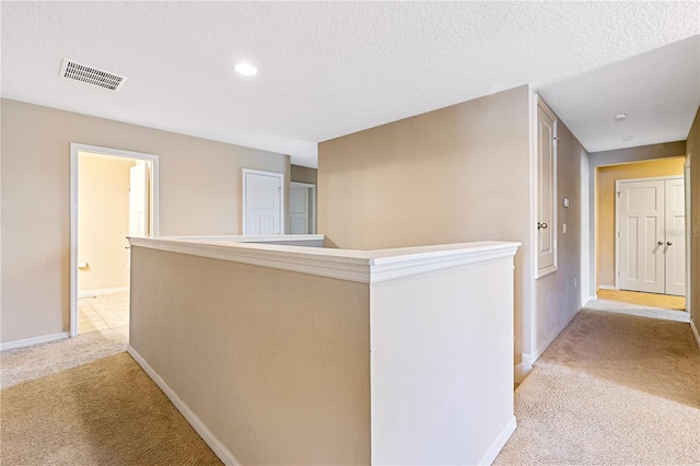 hallway featuring a textured ceiling and light carpet