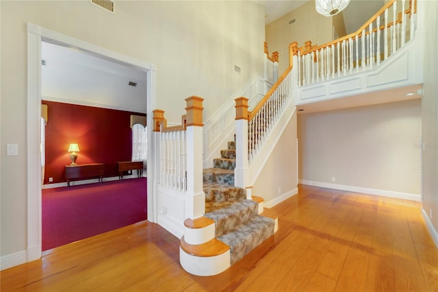 staircase featuring visible vents, wood finished floors, a towering ceiling, and baseboards