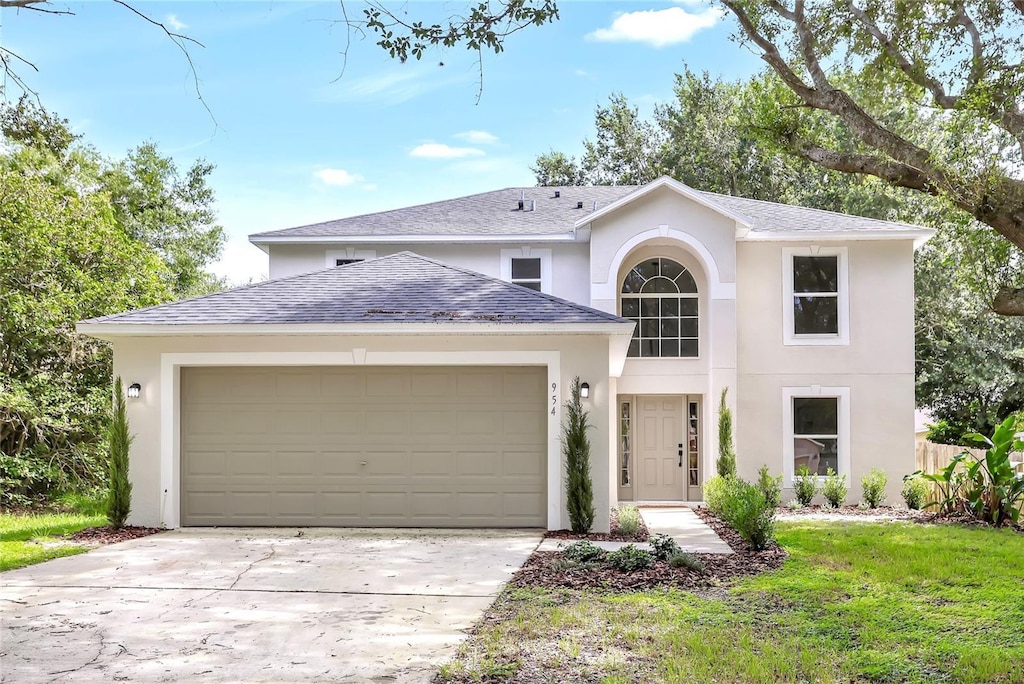 traditional home with concrete driveway, a front yard, an attached garage, and stucco siding