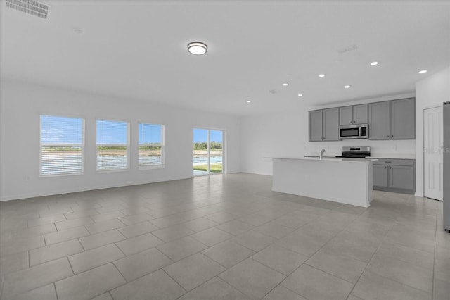 kitchen with stove, an island with sink, light tile patterned floors, and gray cabinets