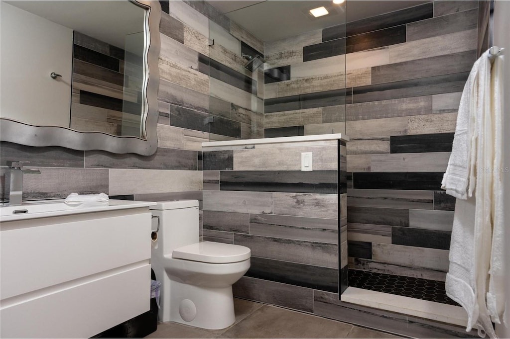 bathroom with toilet, tile patterned flooring, tile walls, vanity, and tiled shower