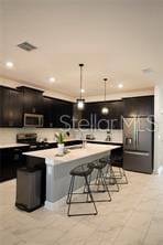 kitchen with a kitchen breakfast bar, pendant lighting, stainless steel refrigerator with ice dispenser, a center island with sink, and light tile patterned flooring