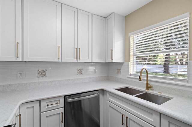 kitchen featuring light stone countertops, white cabinets, dishwasher, sink, and backsplash