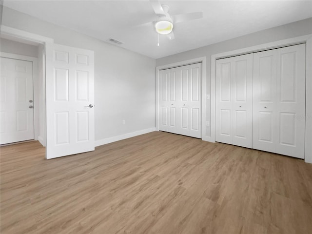 unfurnished bedroom with multiple closets, visible vents, light wood-style floors, ceiling fan, and baseboards