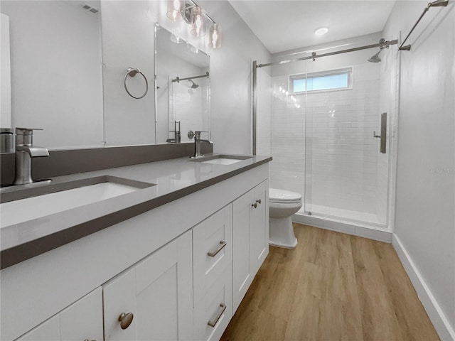 bathroom featuring a shower with shower door, dual vanity, toilet, and wood-type flooring