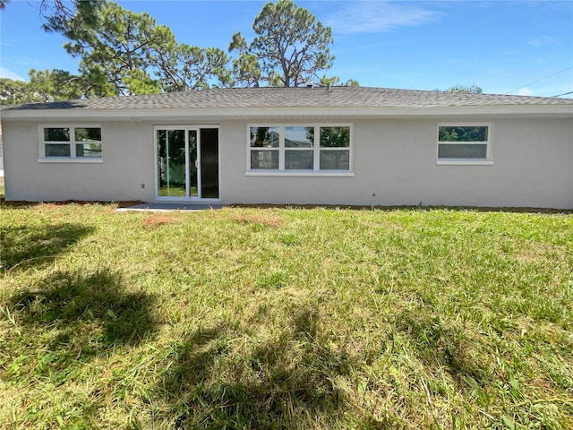 rear view of property featuring a shingled roof, a lawn, and stucco siding