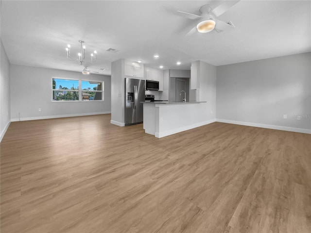 kitchen featuring a peninsula, white cabinets, open floor plan, appliances with stainless steel finishes, and decorative light fixtures