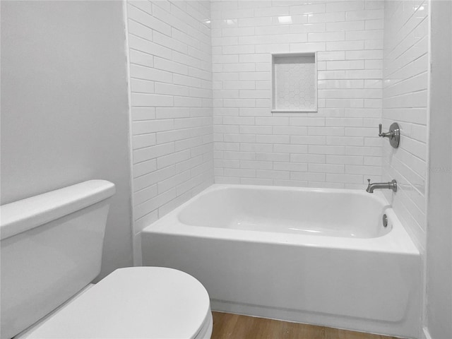 bathroom featuring wood-type flooring, tiled shower / bath, and toilet