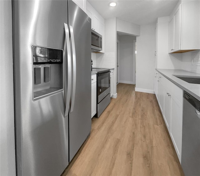 kitchen featuring light wood-type flooring, stainless steel appliances, white cabinetry, sink, and decorative backsplash