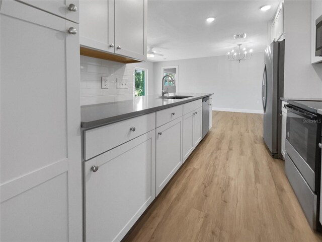 kitchen with stainless steel appliances, decorative backsplash, light wood-type flooring, sink, and white cabinetry