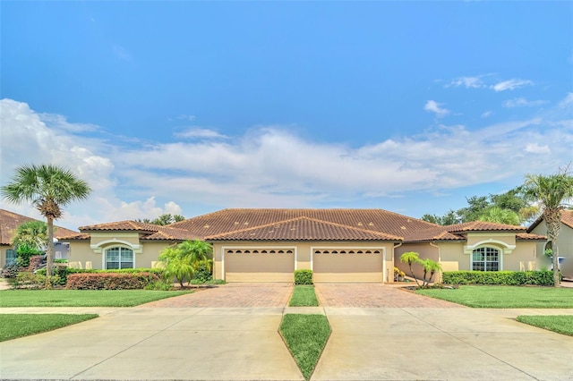 mediterranean / spanish home with a garage, a front lawn, decorative driveway, and stucco siding