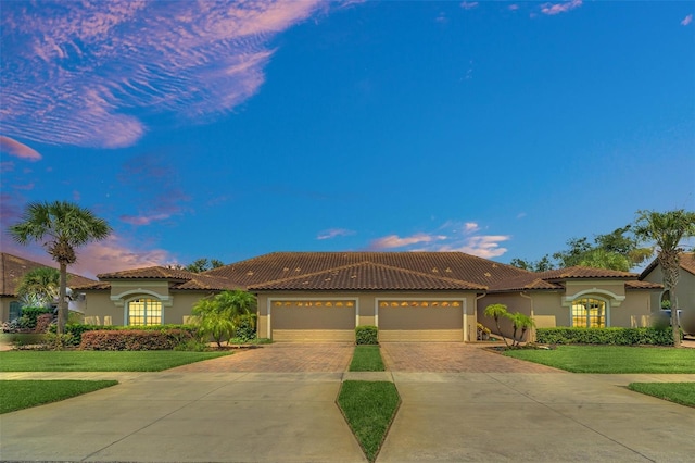 mediterranean / spanish home with decorative driveway, an attached garage, a front yard, and stucco siding