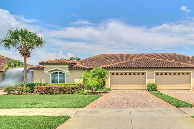 mediterranean / spanish-style house with a front yard, decorative driveway, a tiled roof, and stucco siding