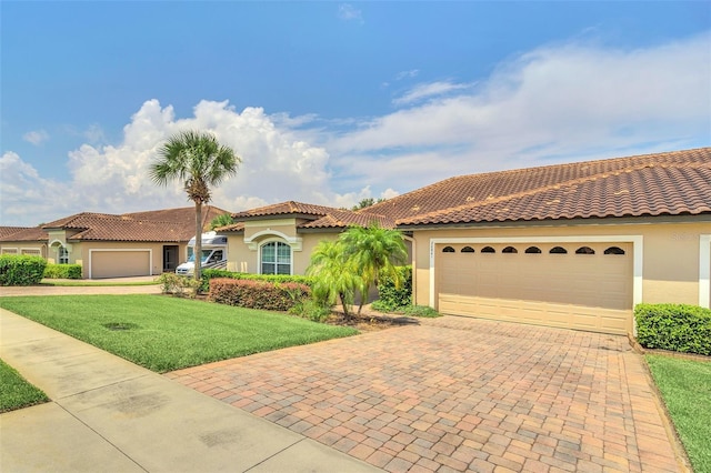 mediterranean / spanish house featuring decorative driveway, a tile roof, stucco siding, an attached garage, and a front lawn