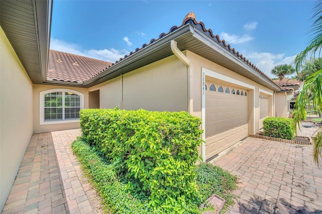 view of property exterior featuring an attached garage, a tile roof, and stucco siding