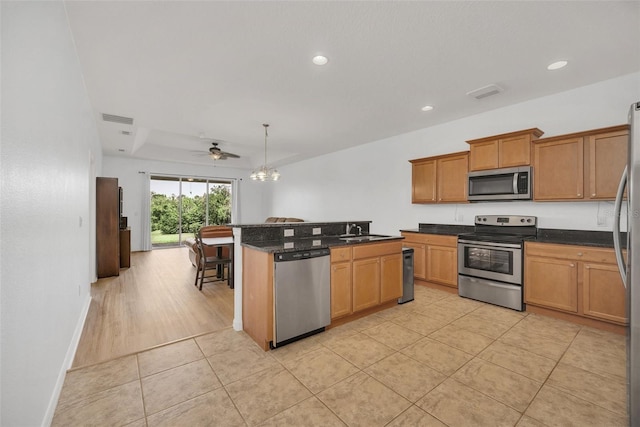 kitchen with light tile patterned floors, stainless steel appliances, a sink, brown cabinets, and decorative light fixtures