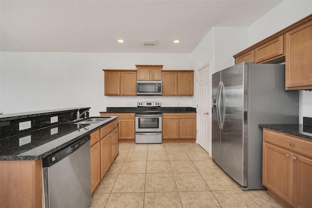 kitchen with appliances with stainless steel finishes, brown cabinetry, dark stone countertops, and a sink