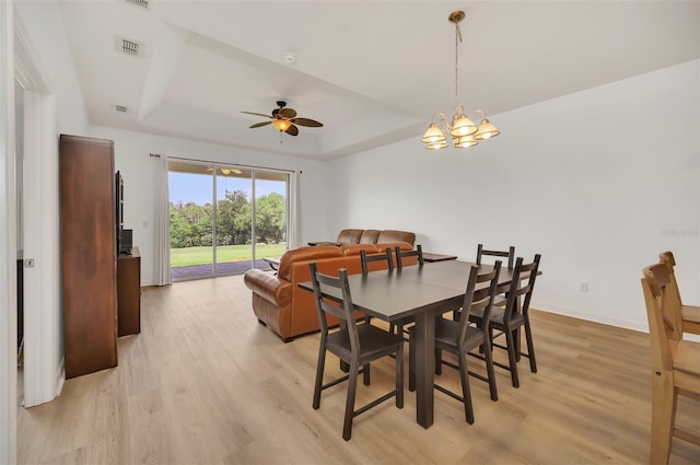 dining area featuring ceiling fan with notable chandelier, a tray ceiling, and light wood-type flooring