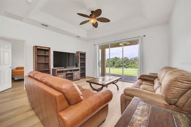 living room with ceiling fan, light hardwood / wood-style floors, and a tray ceiling