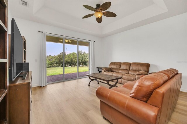 living room with ceiling fan, light hardwood / wood-style flooring, and a tray ceiling