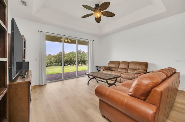 living area with a raised ceiling, visible vents, light wood-style floors, a ceiling fan, and baseboards