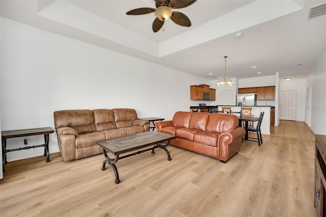 tiled living room with ceiling fan with notable chandelier and a raised ceiling