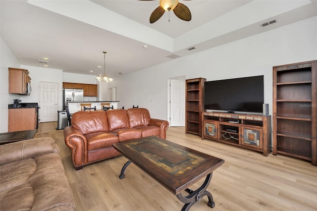 living room featuring ceiling fan with notable chandelier, visible vents, and light wood-style floors