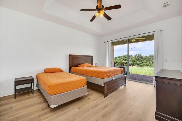 bedroom with ceiling fan, access to outside, light hardwood / wood-style floors, and a tray ceiling