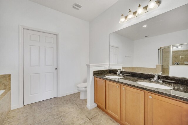 bathroom with dual vanity, toilet, tile patterned floors, and tiled tub