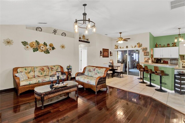 living room featuring ceiling fan with notable chandelier, light wood-type flooring, and vaulted ceiling