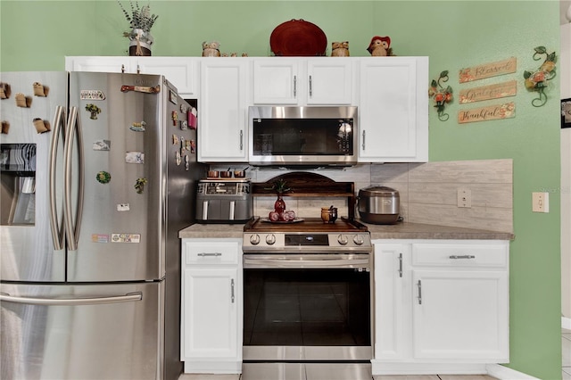 kitchen featuring tile patterned flooring, decorative backsplash, stainless steel appliances, and white cabinetry