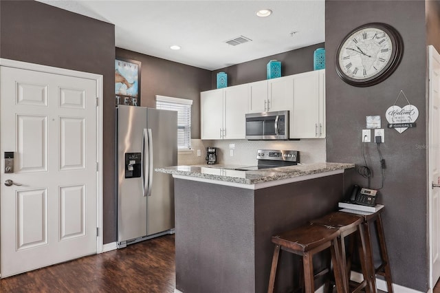 kitchen with appliances with stainless steel finishes, stone countertops, white cabinets, dark hardwood / wood-style flooring, and a kitchen breakfast bar