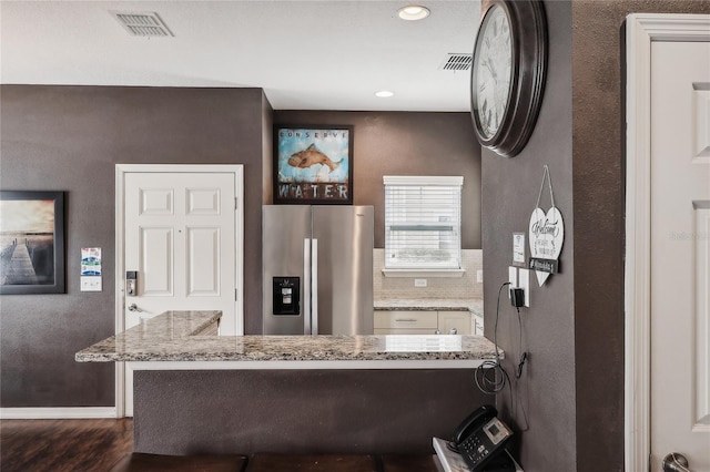 kitchen featuring dark hardwood / wood-style flooring, tasteful backsplash, kitchen peninsula, light stone counters, and stainless steel fridge with ice dispenser