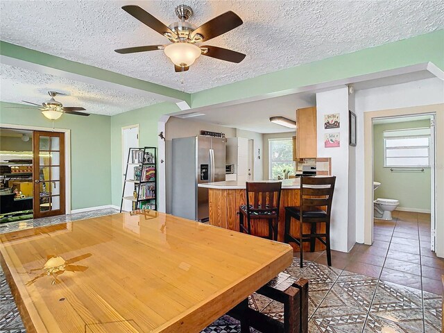 tiled dining area with ceiling fan, a textured ceiling, and a healthy amount of sunlight