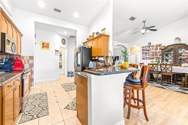 kitchen with lofted ceiling, stainless steel appliances, ceiling fan, light hardwood / wood-style flooring, and kitchen peninsula