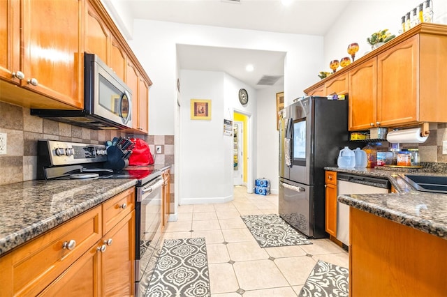 kitchen featuring light tile patterned floors, appliances with stainless steel finishes, dark stone countertops, and backsplash