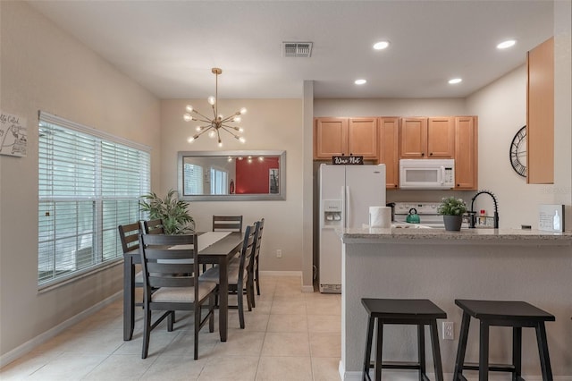 kitchen featuring light stone counters, light tile patterned floors, an inviting chandelier, white appliances, and sink