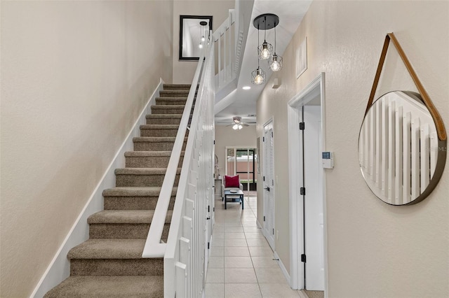 stairway with tile patterned flooring, ceiling fan, and a high ceiling