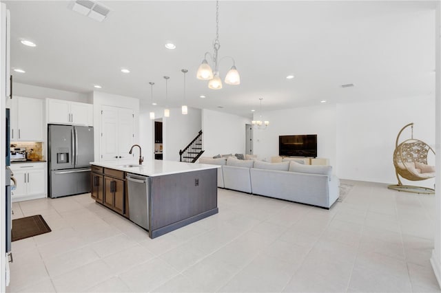 kitchen with sink, a notable chandelier, white cabinetry, stainless steel appliances, and a kitchen island with sink