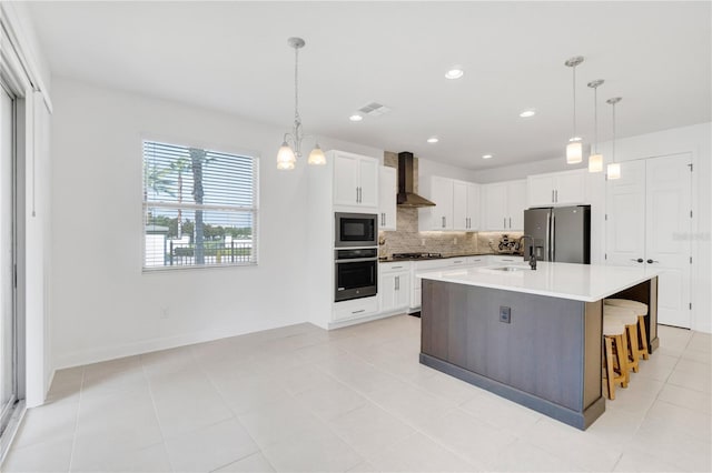 kitchen with white cabinetry, a kitchen island with sink, black appliances, sink, and wall chimney exhaust hood