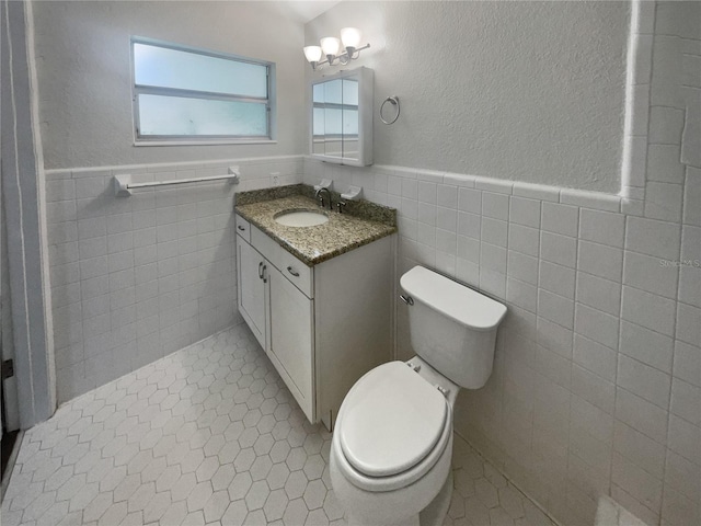 bathroom with tile patterned flooring, toilet, a wainscoted wall, vanity, and tile walls